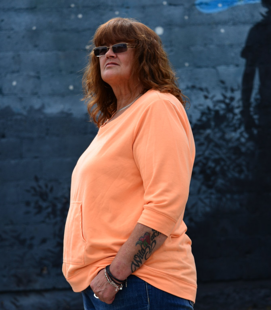 a woman with light brown hair and sunglasses wearing a pastel orange shirt