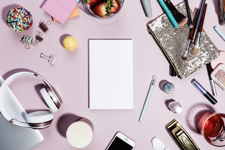 aerial view of a workspace with makeup and headphones and fruit and desk supplies