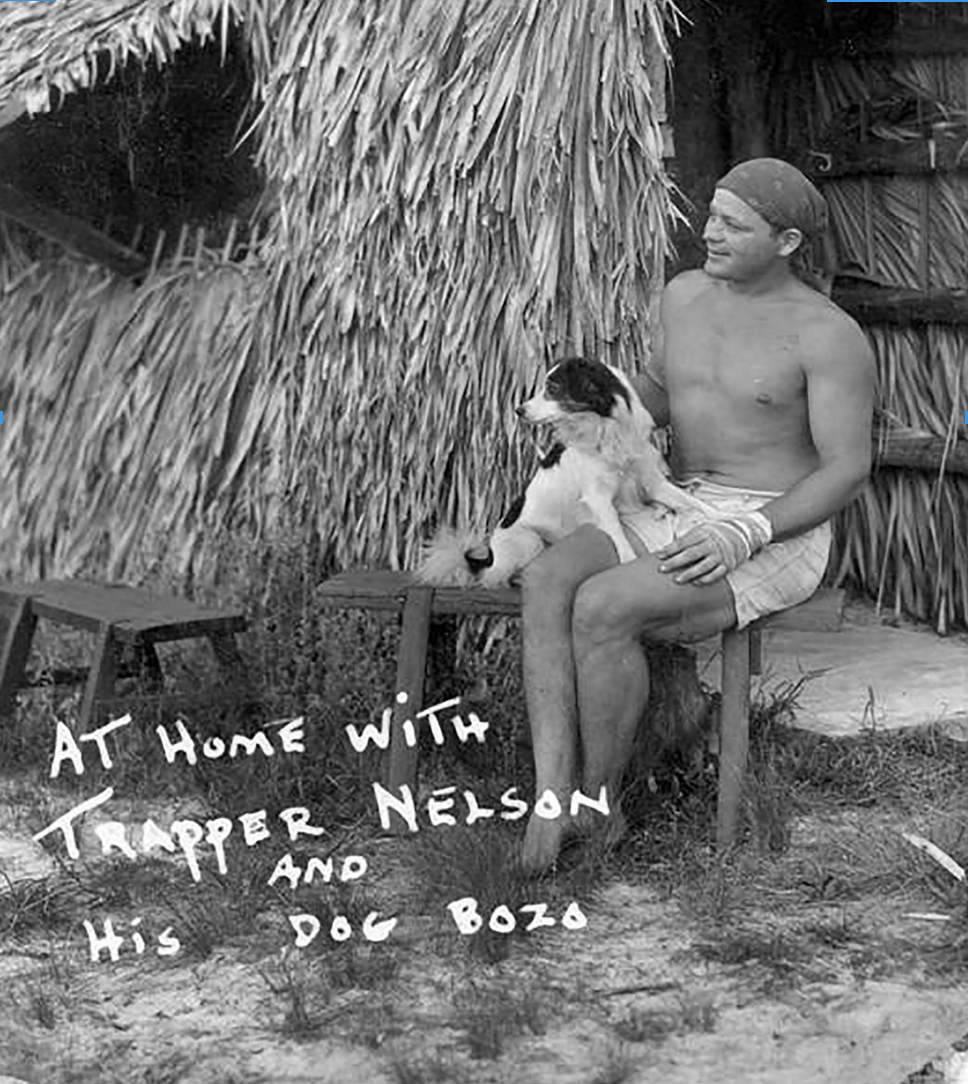 a shirtless man with his dog in front of a straw hut