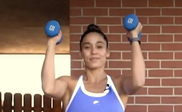 person standing with feet under shoulders, soft bend in knees, holding a pair of dumbbells at chin height, arms narrow in front of body and bent, palms facing inward