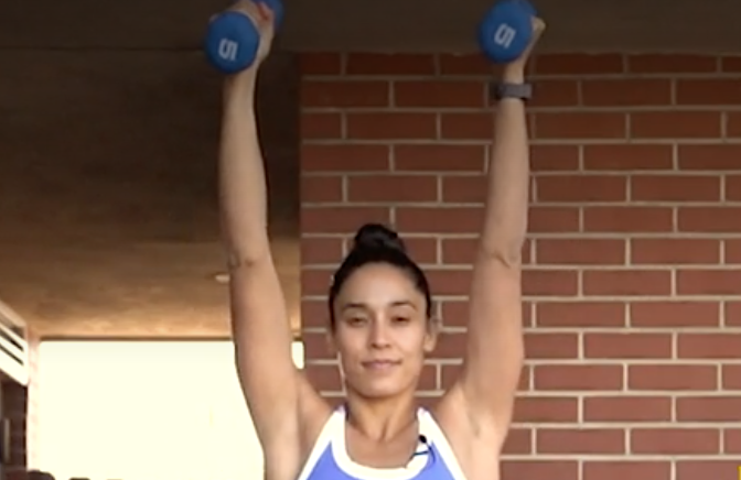 person standing with feet under shoulders, soft bend in knees, holding a pair of dumbbells straight up, arms narrow in front of body and bent, palms facing inward