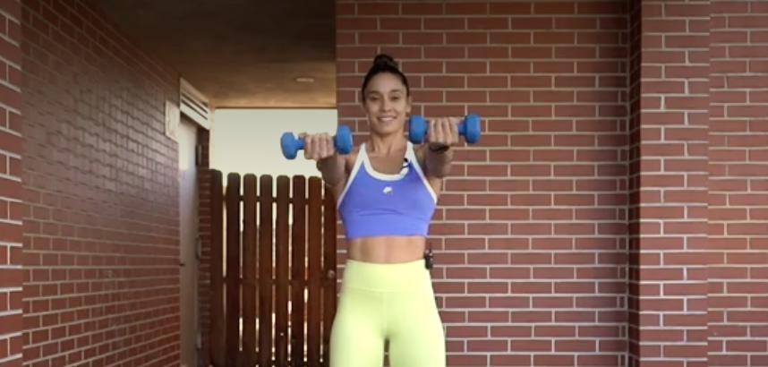 person standing with feet shoulder-width apart holding a dumbbell in each hand, arms straight, palms facing up, weights extended to shoulder level
