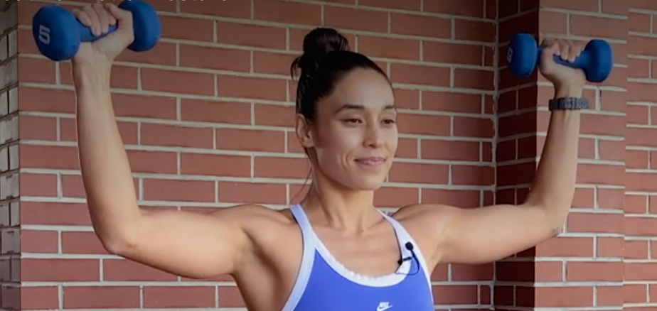 person standing with dumbbells in each hand, elbows bent 90 degrees, in line with shoulders, and dumbbells raised to head height