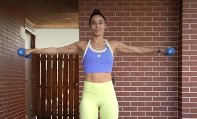 person standing with legs shoulder-width apart, holding a dumbbell in each hand, arms extended out to sides at shoulder height, palms facing floor, making small, clockwise circles with arms