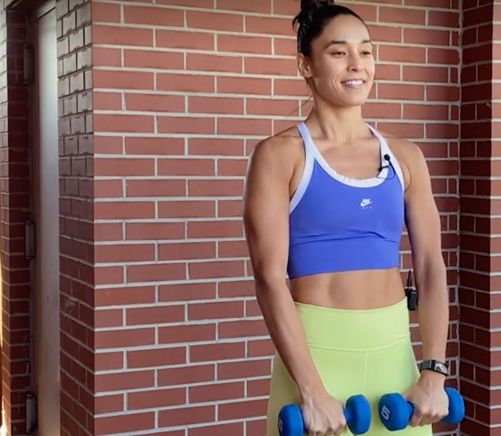person standing with feet shoulder-width apart holding a dumbbell in each hand, arms straight, palms facing body, weights resting on quads