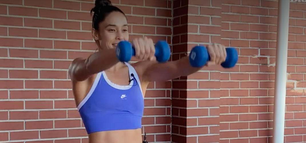 person standing with feet shoulder-width apart holding a dumbbell in each hand, arms straight, palms facing body, weights held straight up at shoulder height