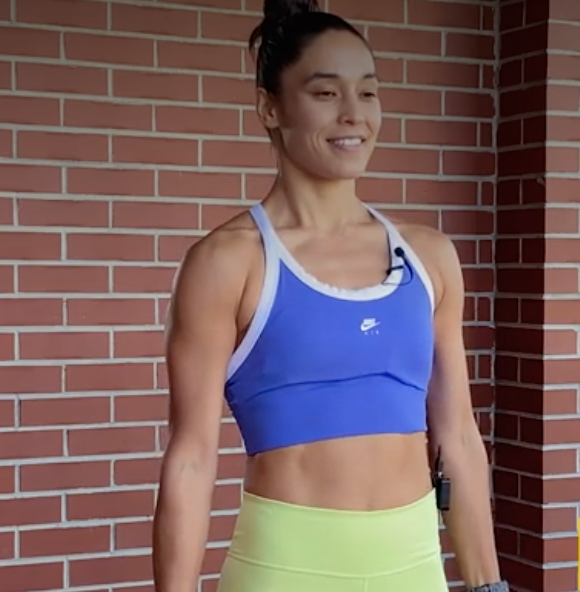 person standing with feet shoulder-width apart, a dumbbell in each hand, and hands at sides.