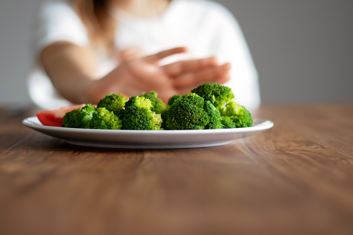 a hand pushing a plate of veggies away 