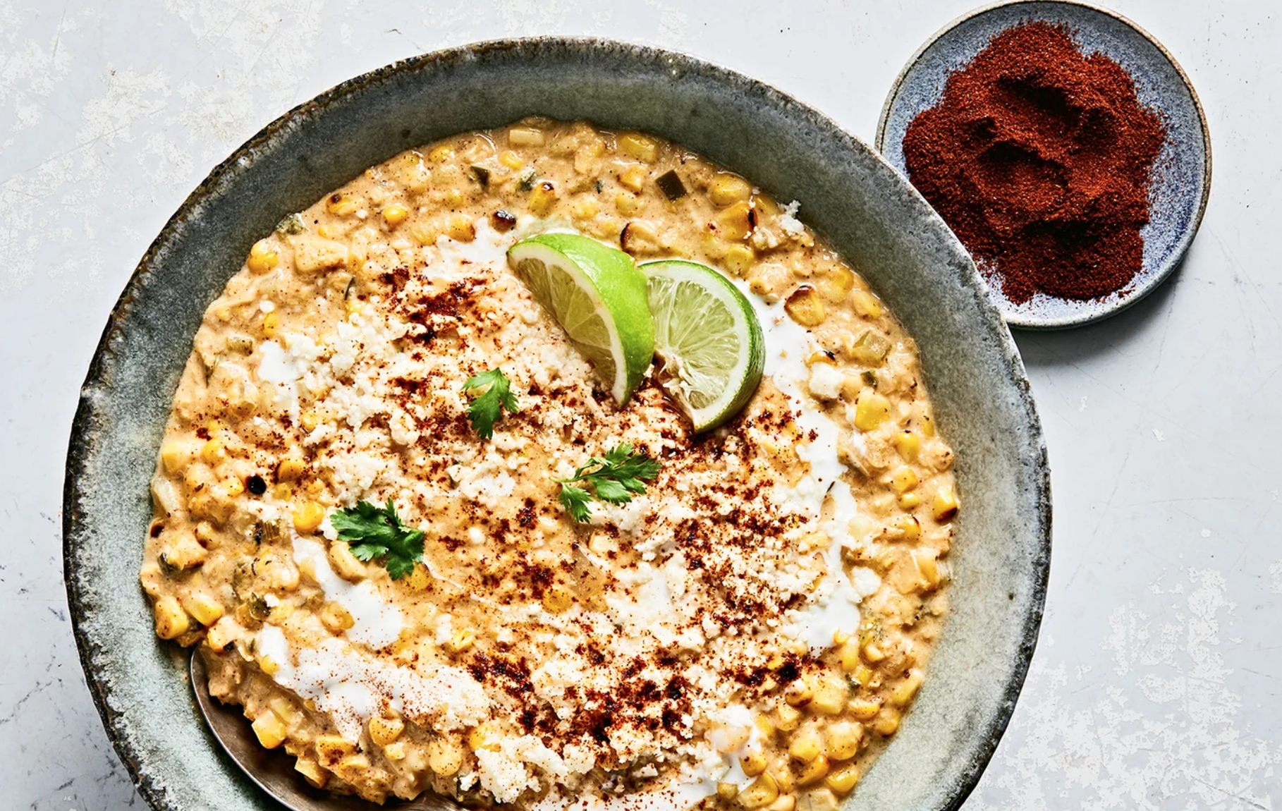 a bowl of corn soup with garnish and a side of seasoning 