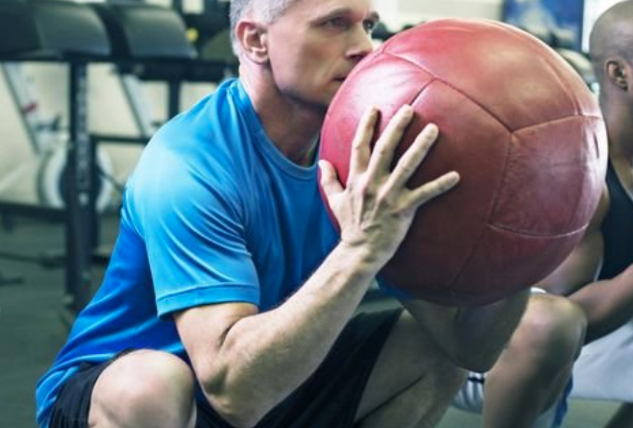 a person squatting a holding a medicine ball