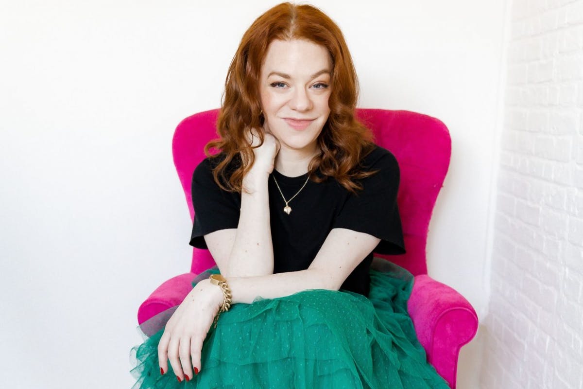 a smiling, stylish person sitting in a hot pink armchair