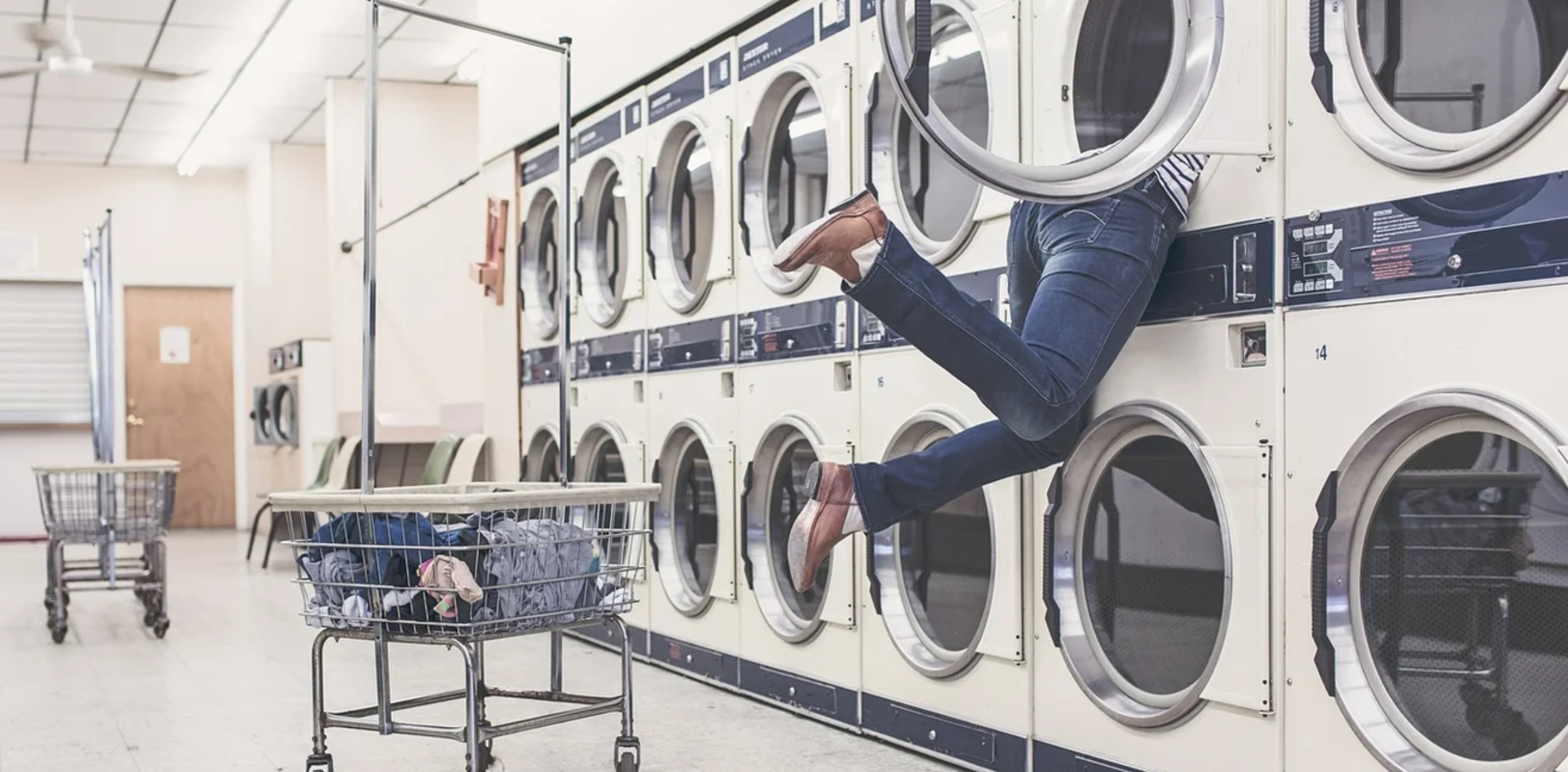 person hanging out of a washing machine in a laundomat