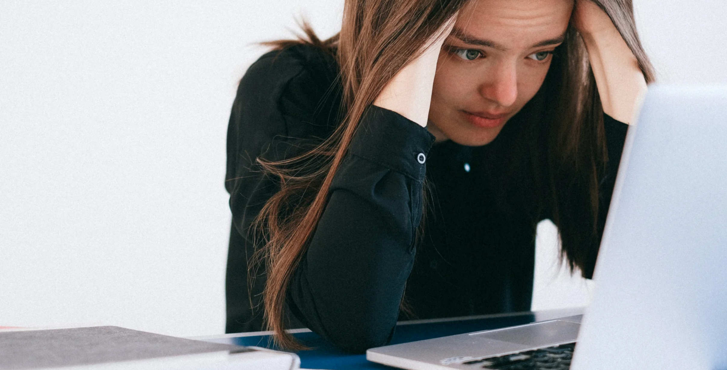 person holding head in hands while staring at a laptop