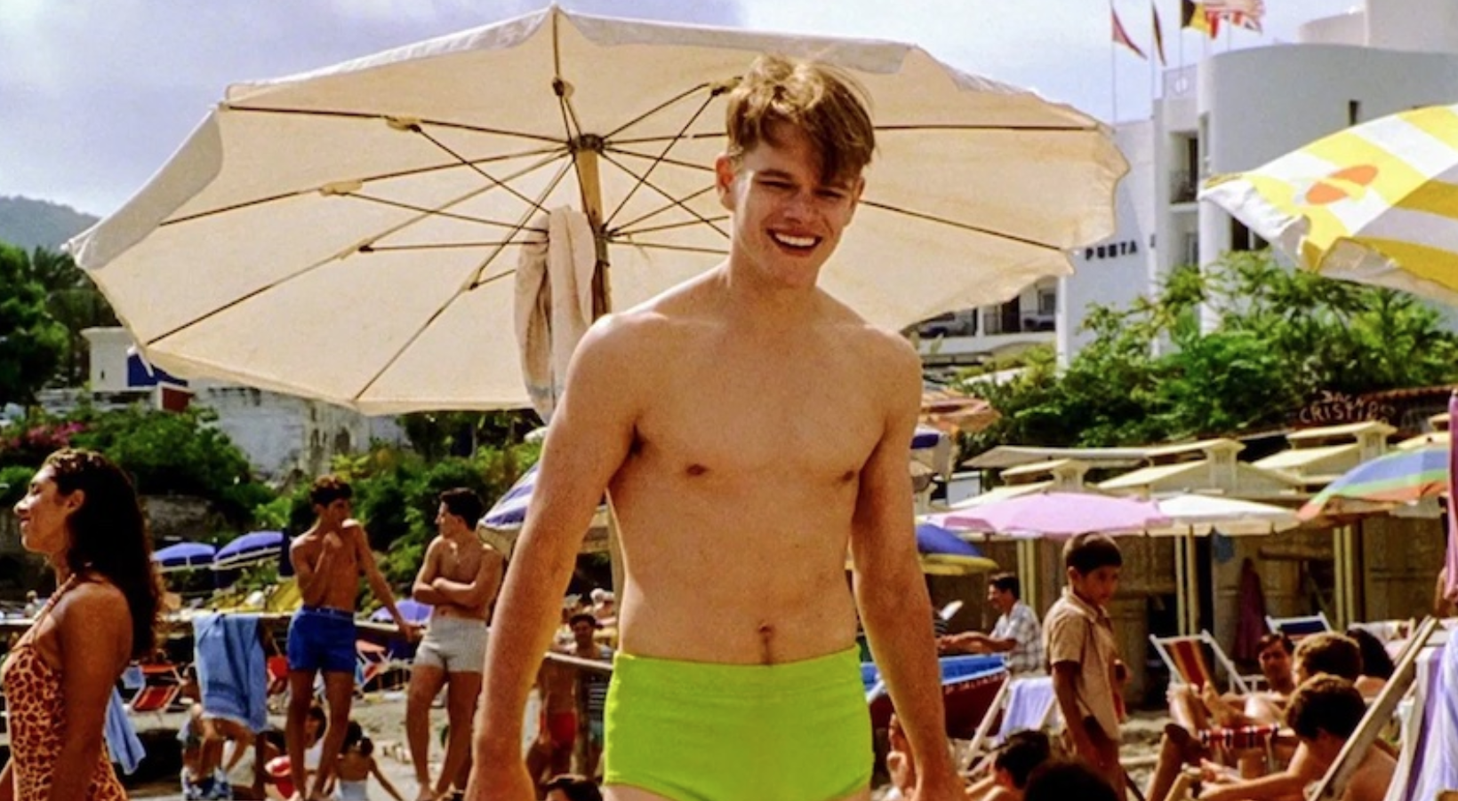 a shirtless man smiling on a crowded beach