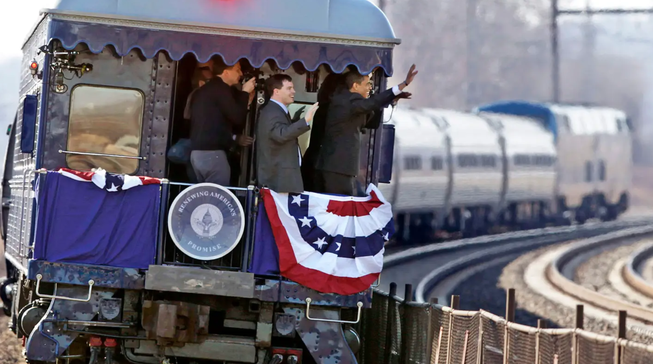 people waving from a train to a crowd off camera