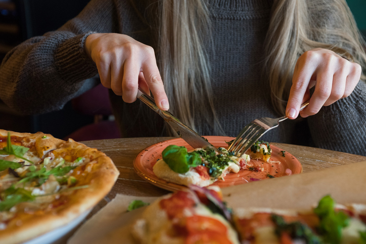 woman eating pizza with a fork and knife