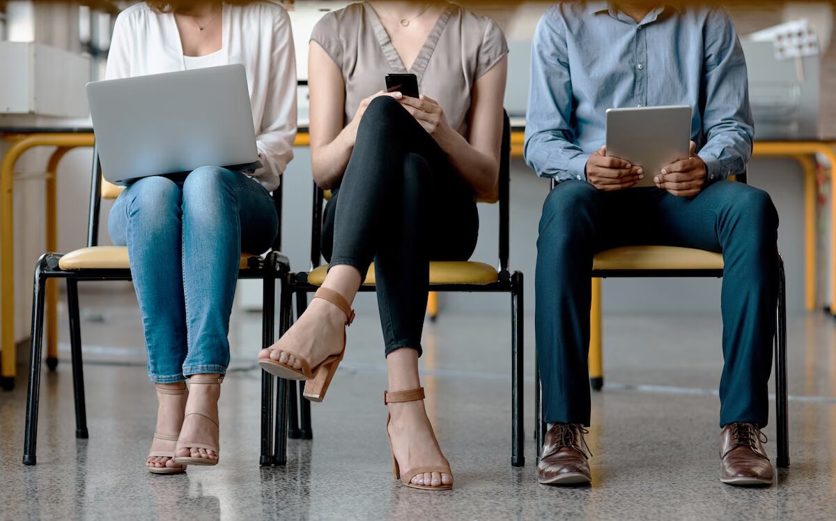 Two women sitting side by side, one on laptop and other on phone 