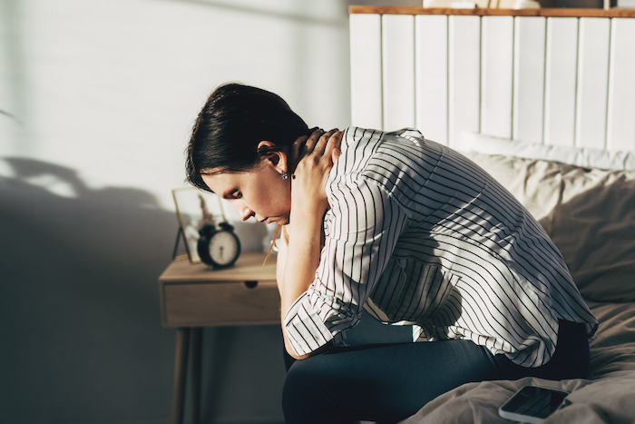 woman sitting on edge of bed looking regretful