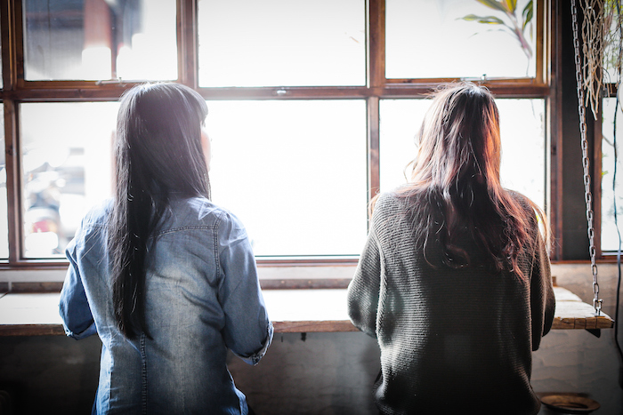 two women sitting in cafe, facing a window