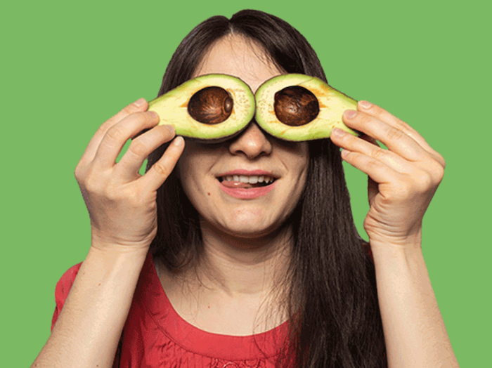 woman holding two avocado halves in front of her eyes